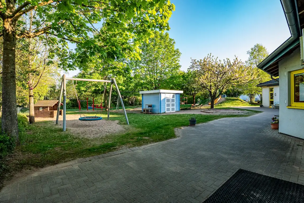 Außenspielplatz der Kita Schweich mit Nestschaukel, Spielhaus und Bäumen