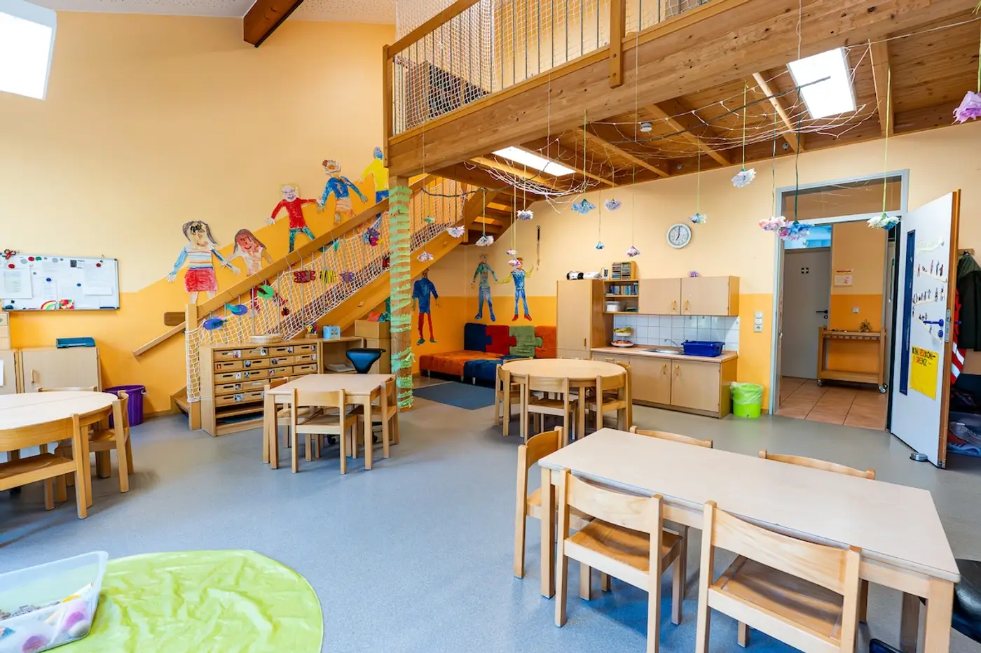 Gruppenraum der Gruppe 6 mit Holz-Hochebene, Treppe und gemalten Kinderfiguren in der Kita Schweich